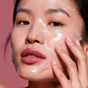 Femme portant un masque visage en tissu transparent et ajustant le masque sur sa joue avec les doigts.