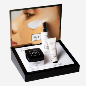 Présentoir 1944 Paris de soins visage et base de teint, devant un visuel de peau hydratée et éclatante.