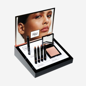 1944 Paris display of cream eyeshadows, pencils and illuminators, in front of a warm, luminous make-up display.