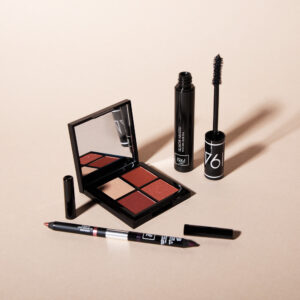 Bộ trang điểm 1944 Paris với phấn mắt, mascara đen và bút chì kẻ mắt trên nền màu be tối giản.