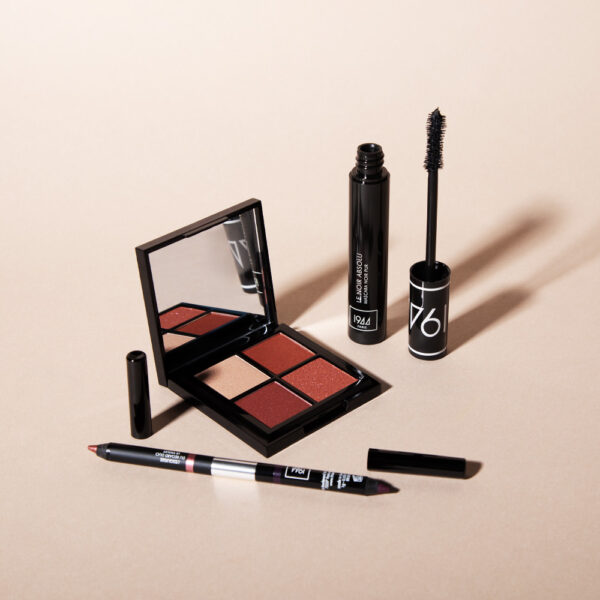 Bộ trang điểm 1944 Paris với phấn mắt, mascara đen và bút chì kẻ mắt trên nền màu be tối giản.