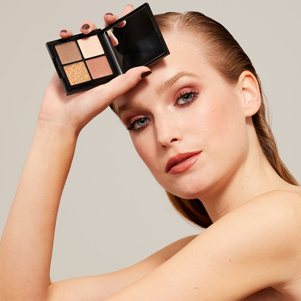 Mannequin tenant une palette d’ombres à paupières 1944 Paris aux teintes chaudes et irisées.