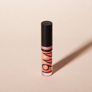 1944 Paris luminous lip gloss in a transparent tube, presented on a minimalist beige background.