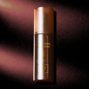 1944 Paris Bronzing Tinted Water-flaska med strukturerad brun bakgrund, varm belysning som framhäver produktens bärnstensfärgade finish.