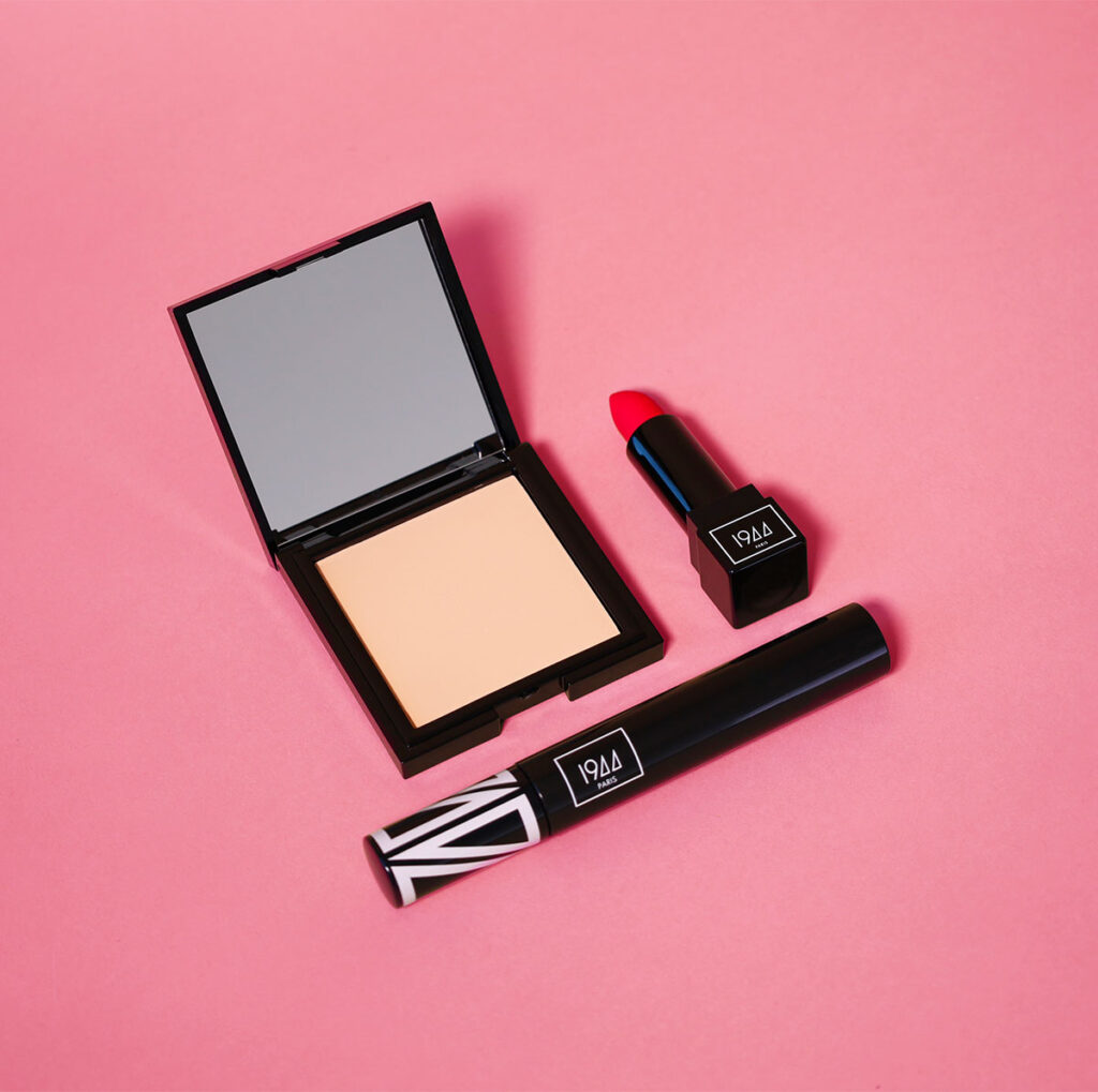 Produits coffret icône intemporelle 1944 Paris rouge à lèvres mat, mascara et poudre matifiante disposés sur fond rose
