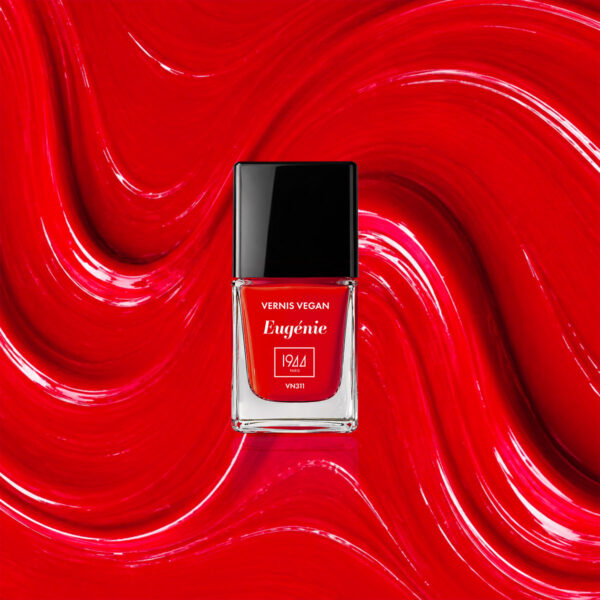 Flacon du vernis vegan Eugénie VN311 1944 Paris sur une texture rouge éclatante.