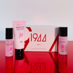 Coffret Le Rituel Éclat 1944 Paris : étui blanc et rouge avec Le Baume Démaquillant, La Sublime Glow crème haute hydratation et Le Soin Éclat crème yeux de la gamme Pink V Collagen, sur une surface rouge brillante