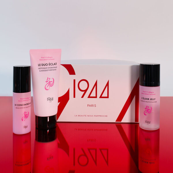 Coffret Le Rituel Éclat 1944 Paris : étui blanc et rouge avec Le Baume Démaquillant, La Sublime Glow crème haute hydratation et Le Soin Éclat crème yeux de la gamme Pink V Collagen, sur une surface rouge brillante