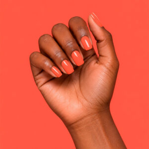 Main à la peau foncée portant le gel semi-permanent vegan Coraline corail orangé, sur fond corail orangé