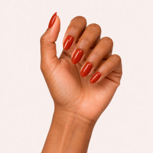 A hand with a matte finish, wearing Maella’s orange-red vegan semi-permanent nail varnish, against a beige-pink background