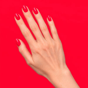 Main à la peau claire portant le gel semi-permanent vegan Adrienne rouge, sur fond rouge vif