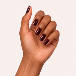 Main à la peau mate portant le gel semi-permanent vegan Nine bordeaux foncé, sur fond rose pâle