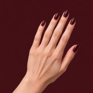 Main à la peau claire portant le gel semi-permanent vegan Nine bordeaux foncé, sur fond bordeaux foncé
