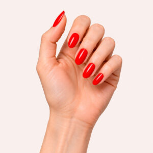A hand with fair skin, wearing the vegan semi-permanent nail varnish ‘Eugénie’ in intense red, against a pale pink background