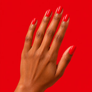A hand with a matte finish, wearing the vegan semi-permanent nail varnish ‘Eugénie’ in intense red, against a red background